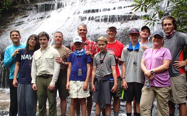 A group of parents and children pose for a group photo in front of a waterfall.